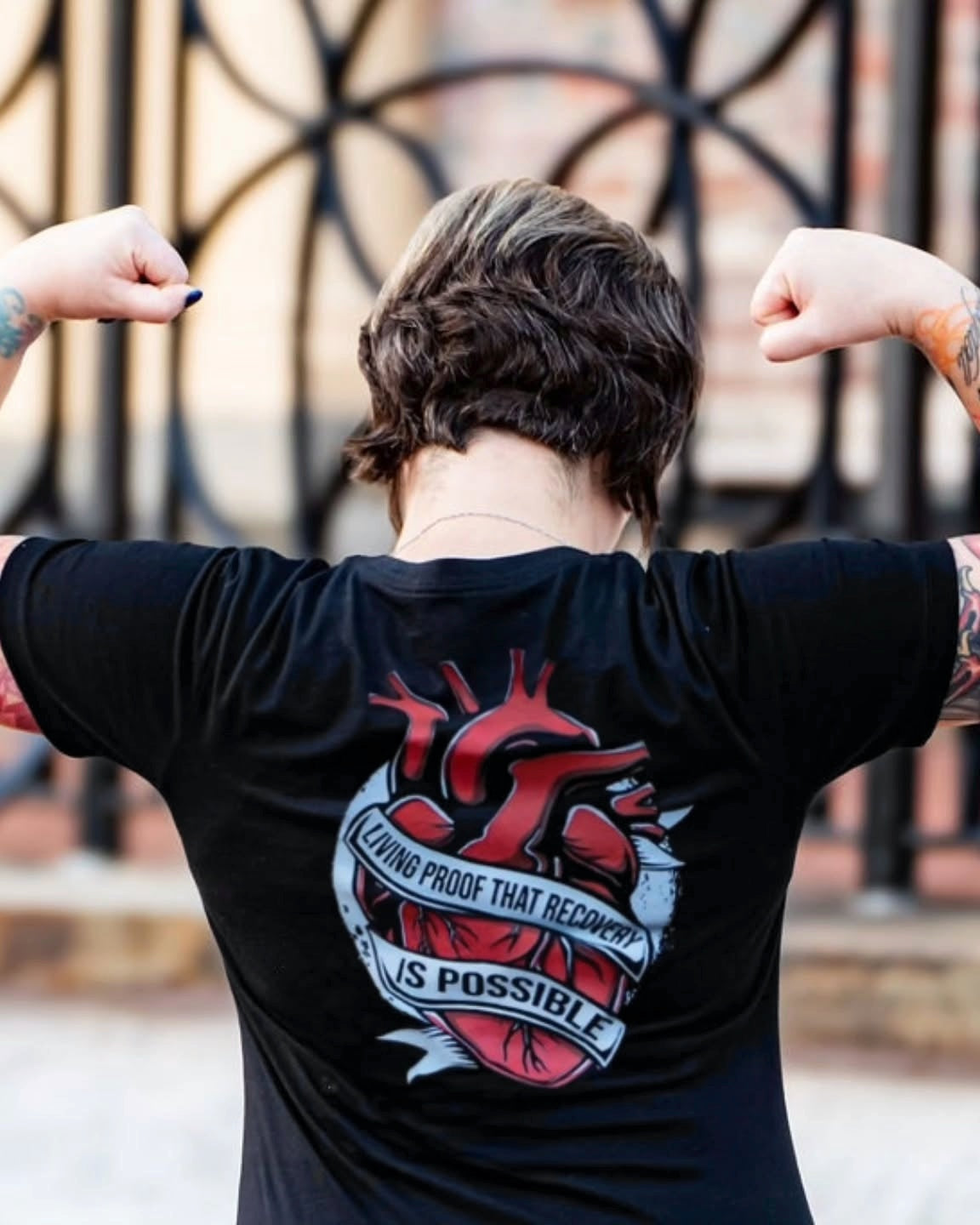 Woman wearing the black Unchained Heart tee, back view showing the heart and banner print